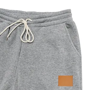Detalle de pantalones de chándal grises para hombre con cordón y parche de cuero