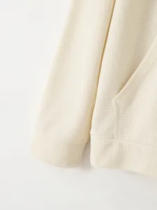 Gros plan sur la texture gaufrée beige du sweat-shirt, détails du poignet et de la poche