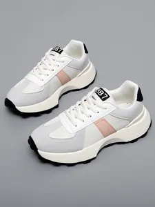 Primo piano di scarpe bianche autunnali con strisce rosa e suole a carrarmato nere su grigio
