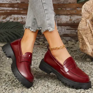 Detailansicht eleganter burgunderroter Lackleder-Plateau-Loafer auf einem Kiesweg