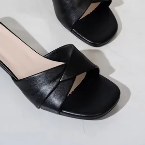 Primer plano de sandalias negras de punta cuadrada con detalle de tira cruzada.