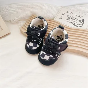 Close-up of black and white checkerboard soft-sole baby walking shoes with bow detail.