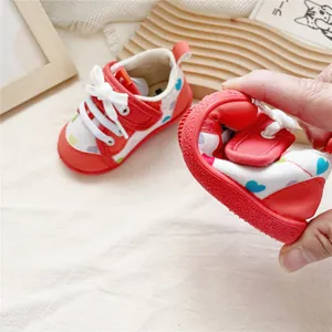Detail of red soft-sole baby walking shoes with heart pattern being bent for flexibility