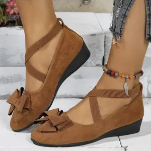 Detail view of brown suede wedge shoes with elegant bow and elastic cross straps