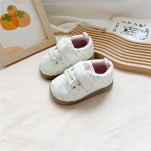 Close-up of white baby walking shoes with colorful heart patterns and soft soles.