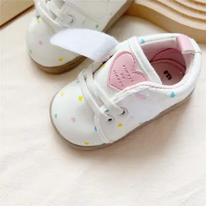 Close-up of white baby shoes with colorful heart prints and pink 'always be HAPPY' patch
