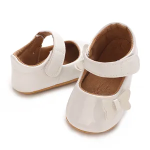 Close-up of white baby girl princess shoes with a delicate bow and Velcro strap.