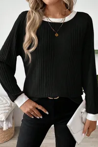 Detail of black ribbed knit sweater featuring white contrast collar and cuffs detail.