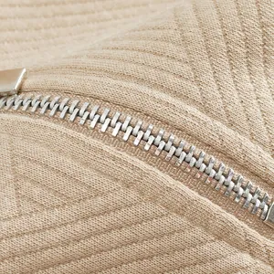 Primer plano de la cremallera metálica plateada y tejido jacquard texturizado de un polo beige