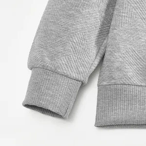 Detalle del tejido jacquard gris pesado y el puño acanalado en una sudadera de hombre