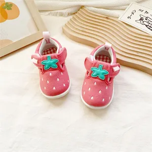 Vue détaillée de chaussures de marche pour bébé roses au design fraise avec velcro vert.