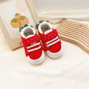 Gros plan de chaussures rouges fraise pour bébé avec pois et bride velcro.