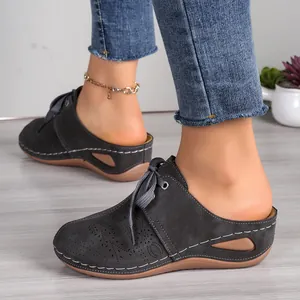Detailed side view of women's dark grey laser-cut lace-up wedge mules worn by a model