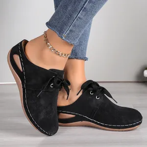 Close-up detail of black lace-up wedge mules with perforated suede design on foot