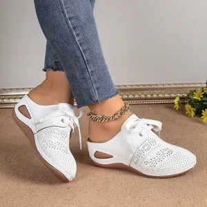 Detail view of white lace-up wedge mule sandals with decorative hollow-out pattern.