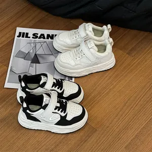 Sneaker casual bianche e nere per bambini su un pavimento in legno con decori.