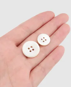 Close-up view of two premium cream shell buttons with textured rims held in hand