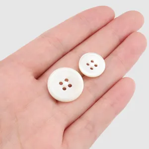 Two white trochus shell buttons with ridged patterns on a hand for scale reference