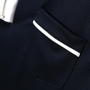 Detailansicht der Brusttasche mit weißer Paspelierung auf dunkelblauem Polo-Shirt.