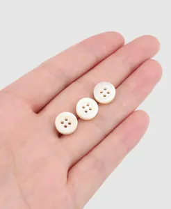 Close-up of three white trochus shell shirt buttons with four holes and etched patterns