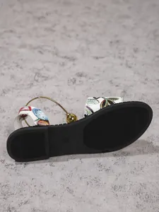 Detailed close-up of women's flat sandal showing black sole and gold ring detail.