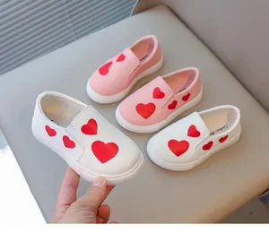 Close-up of girls' white and pink slip-on shoes with red heart patterns and soft soles.