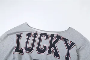 Primer plano del estampado 'LUCKY' en camiseta gris de manga larga con hombros caídos.