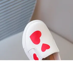Detailed close-up of girls' white leather slip-on loafers with cute red heart print