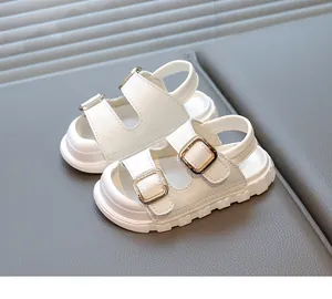 Close-up view of white children's sandals with double gold buckles and thick soles.