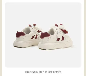 Vista posteriore di sneakers bianche per bambini con fiocco rosso e strisce laterali.