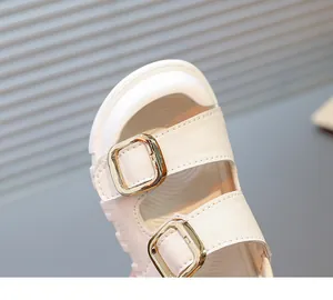 Close-up of children's white leather sandals featuring gold buckle straps and fine stitching