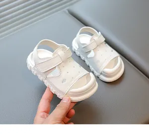 White toddler sandals with soft soles and velcro straps held by hand for detail