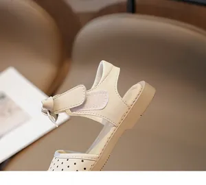 Primer plano de sandalia beige con lunares para niña con un lazo y cierre de velcro.