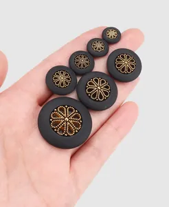 Detailed view of vintage-style black and gold buttons in various sizes held in hand.