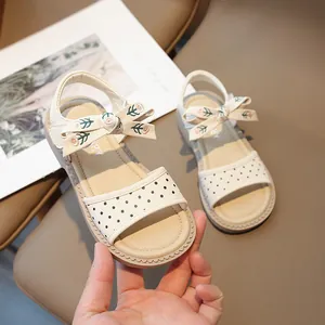 Sandalias de princesa crema para niños con lunares negros y detalle de lazo floral.