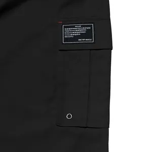 Close-up view of black cargo pants pocket with a custom text patch and silver metal eyelet