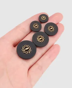Detailaufnahme schwarzer Nylonknöpfe mit goldener Mitte in einer Hand gehalten für Größe