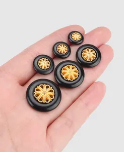 Detailansicht eleganter schwarz-goldener Filigranknöpfe aus Nylon auf einer Handfläche