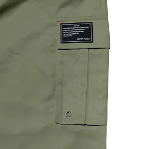 Close-up detail of olive green cargo pants with flap pocket and black woven label.