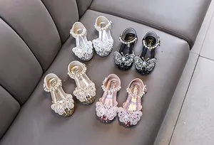 Close-up of glittery girls princess shoes with butterfly diamond decor and pearl ankle straps.
