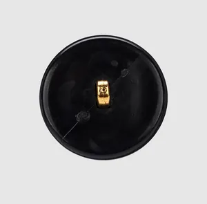 Close-up back view of a black round nylon button with a gold-tone metal sewing shank