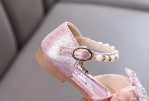 Close-up of girls' pink glitter shoes featuring elegant pearl strap and gold buckle