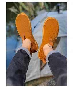 Top-down view of lightweight brown barefoot hiking shoes worn outdoors near a tent.
