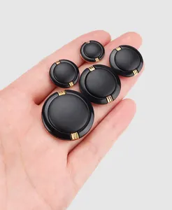 Detailed view of high-end black buttons with gold accents in various sizes held by a hand