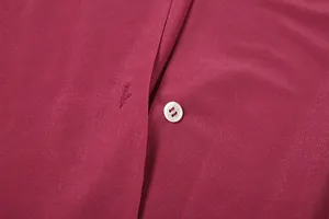 Dettaglio macro di un bottone bianco e trama del tessuto bordeaux su un abito elegante