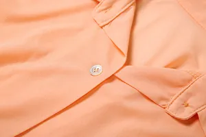 Dettaglio ravvicinato dell'abito a camicia color pesca con trama del tessuto e bottone