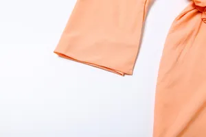 Dettaglio ravvicinato del tessuto arancione liscio e dell'orlo della manica di un abito a camicia