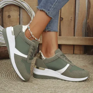 Detailed view of women's olive green wedge sneakers with gold accents on a woven mat