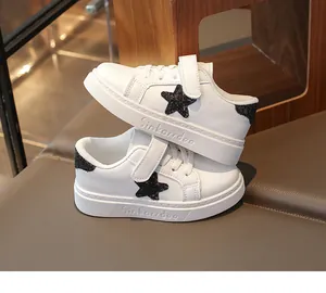 Close-up van witte leren kindersneakers met zwarte glitterster en klittenbandsluiting