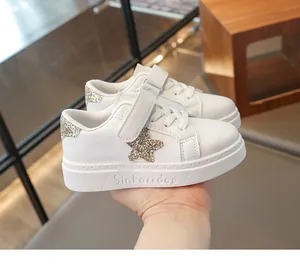 Close-up van witte kindersneakers met glitterende gouden ster en klittenbandsluiting.
